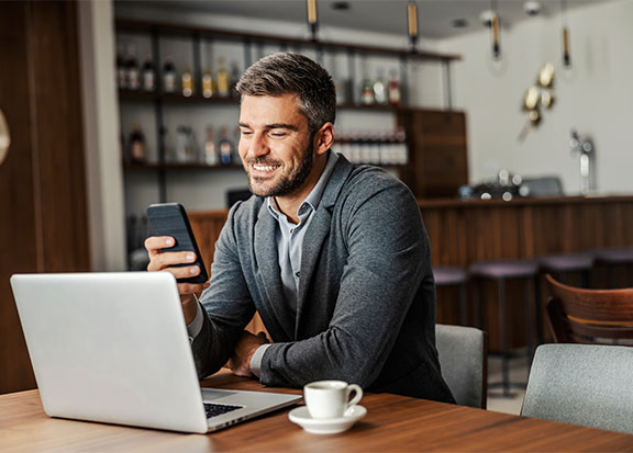 Transaction Management | Person smiling while looking at their phone with their laptop in front of them