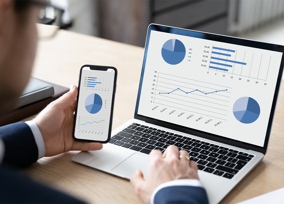 Person looking at laptop and phone, both with metrics and graphs on them