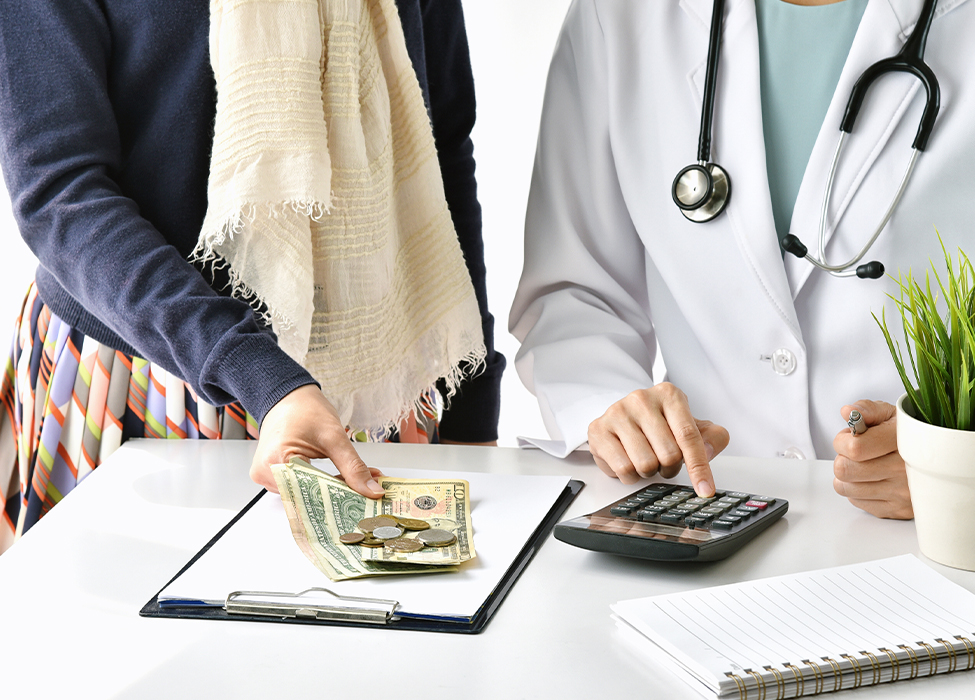 claims adjudication | Close up of two people, one a healthcare professional, talking and looking over papers and a calculator