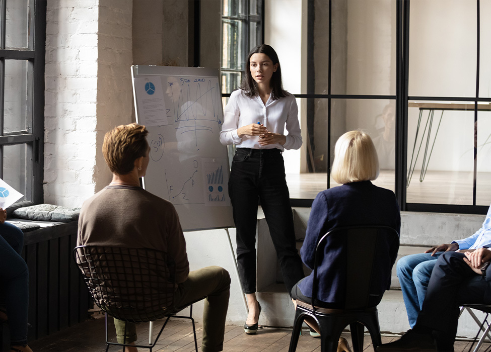 Employee Benefits | Woman stands in front of a seated audience in a workplace training session