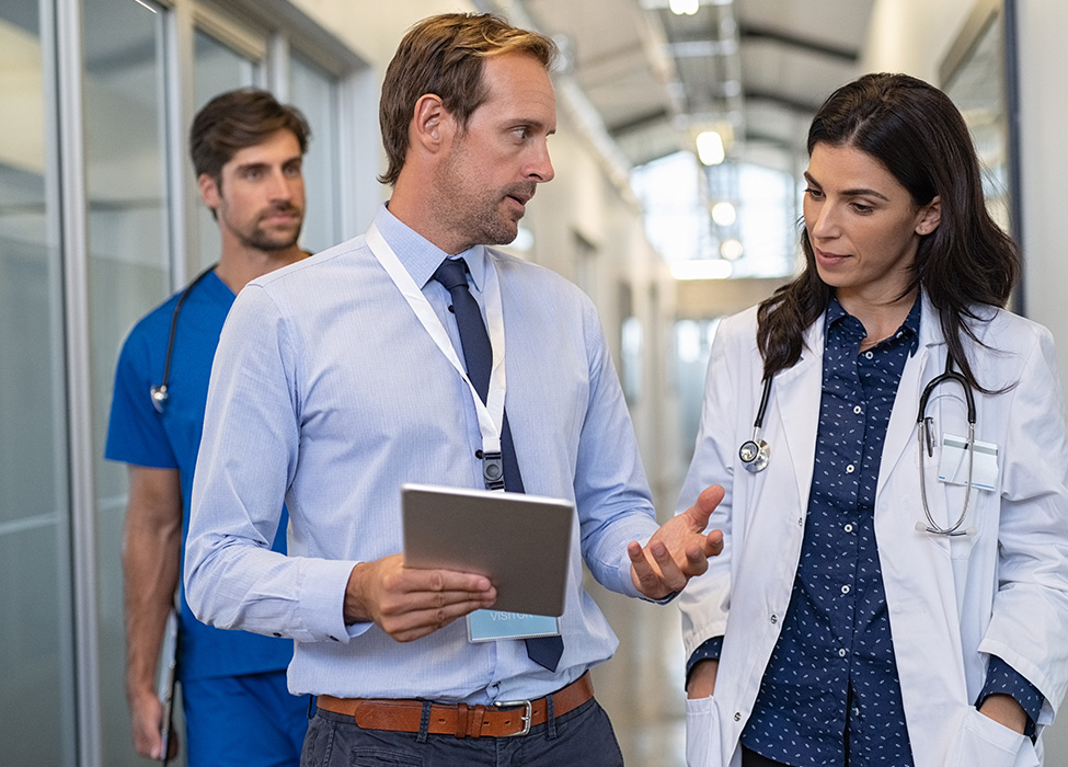 Medical coding solutions | man in suit holding clipboard talks to a female doctor while they walk through a hallway