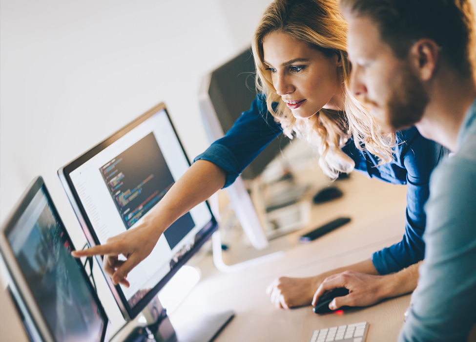 Two people are looking at a screen with one of them pointing toward it